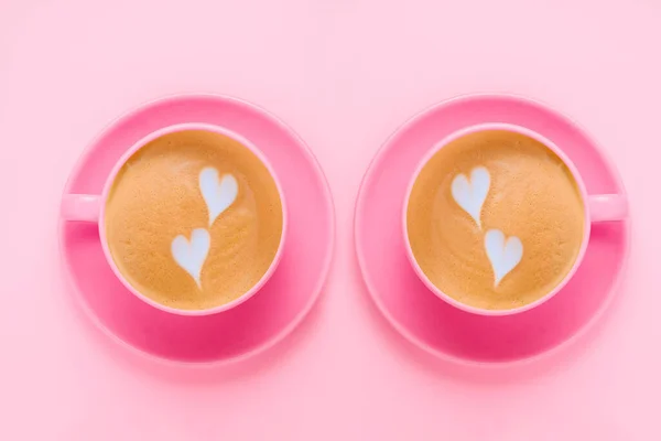 top view flat lay coffee with latte art two  pink cups on a soft pastel pink background, creative minimal card on a pink background