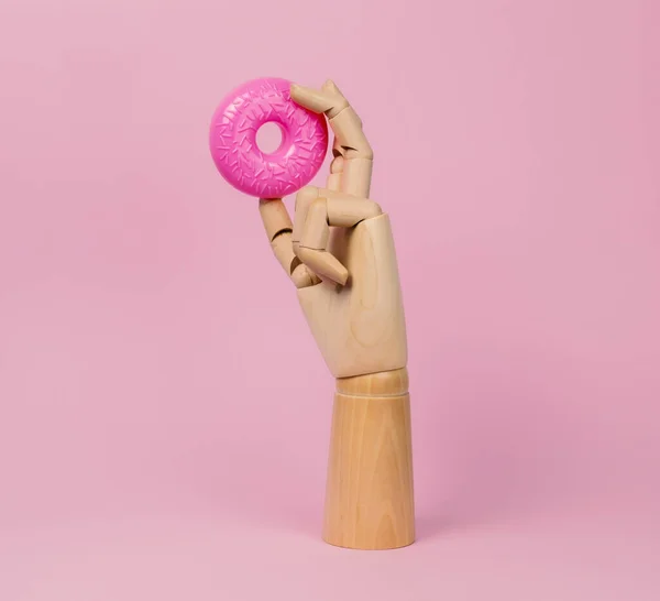 木制的手 粉红的甜甜圈 粉红的背景 假冒伪劣塑料食品和不健康饮食概念 — 图库照片