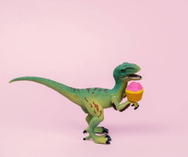 Tatlı yeşil plastik dinozor oyuncağı. Kek desenli, pastel pembe arka planı var..
