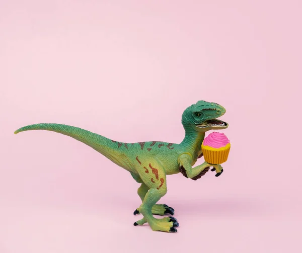 Cute green plastic dinosaur toy with cupcake decorated  pastel pink background.
