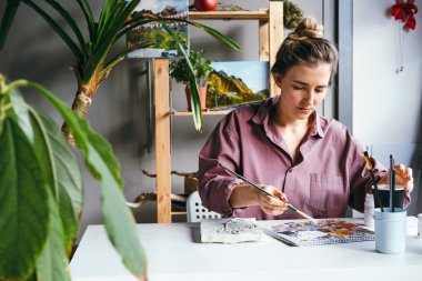 Sanat stüdyosunda bir sürü yeşil bitkiyle resim çizen genç bir kadın. Sanat ve hobi konsepti.