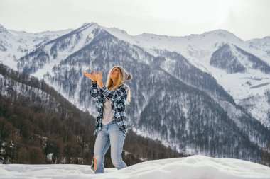 Genç ve güzel bir kadın dağlarda karla oynuyor. Seçici odak.
