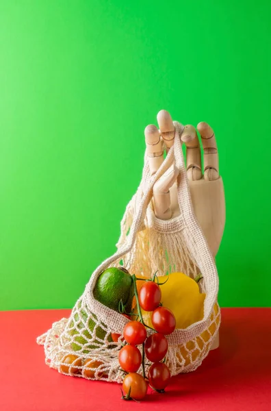 Modern still life with wooden hand,string bag and fresh vegetables on a green red background