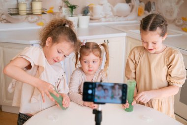 Üç tatlı kız kardeş mutfakta salya sümük oynuyor ve internet günlüğü için video içeriği oluşturuyor.