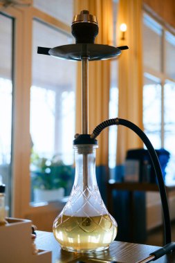 Bulanık bir restoran salonunun arka planında duman olan bir masaya nargile koy. Nargile içmek..