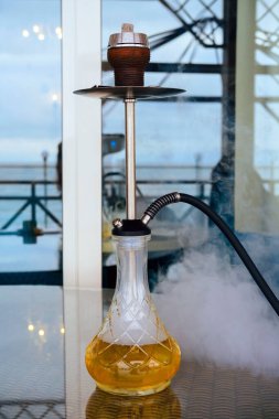 Bulanık bir restoran salonunun arka planında duman olan bir masaya nargile koy. Nargile içmek..