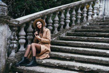 Şapka ve ceket giyen, merdivenlerde oturan güzel genç bir kadın. Seyahat kavramı.