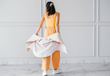 Güzel, genç esmer kadın, kadife gömlek ve bej renkli duvarda spor ayakkabıları olan pamuk bir takım elbise giyer.