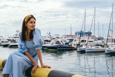 Yatların arkasında kıyıda oturan mavi elbiseli güzel bir kadının portresi. Deniz yolculuğu konsepti.
