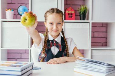 Little girl a school student sits at her desk and holds out an apple