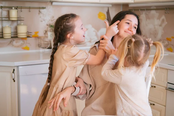 Young mother is sitting in kitchen and two naughty daughters are running around her. Parenting concept.