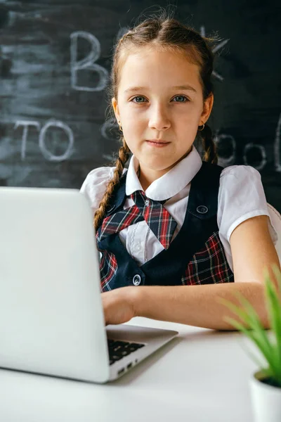 Cute little school girl sitting at the desk and using computer. Back to school and online lessons concept.