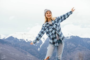 Ekose gömlek, kot pantolon ve örgü şapka giyen güzel sarışın kadın dağlardaki temiz havanın tadını çıkarıyor. Pozitif seyahat kavramı.