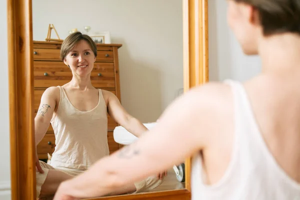 Pamuklu ev kıyafetleri içinde kısa saçlı, güzel ve seksi bir kadın. Gülümsüyor ve aynada kendine bakıyor.