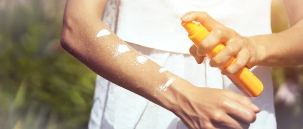 Uma jovem em um vestido branco aplica gel protetor solar para seus braços e ombros. — Fotografia de Stock