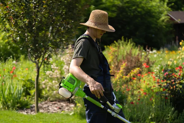 En ung man med gräsklippare tar hand om gräset på bakgården.. — Stockfoto