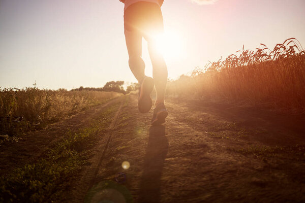 Athlete runner legs running on a close-up of a trail across a field.