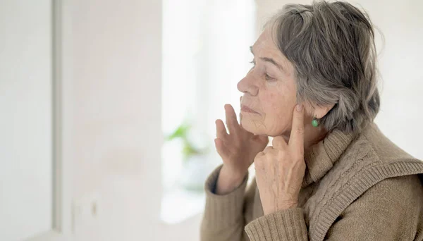 An elderly woman applies an anti-aging moisturizer.