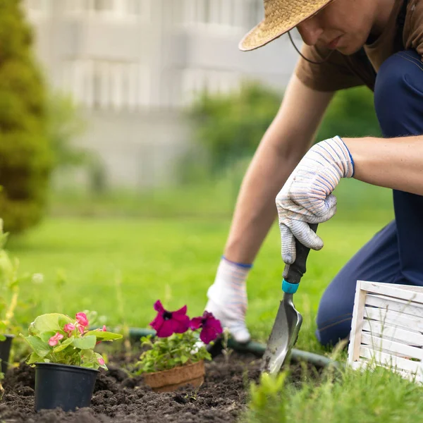 Um jovem em um chapéu de palha e mãos em luvas está envolvido no trabalho de jardinagem. — Fotografia de Stock