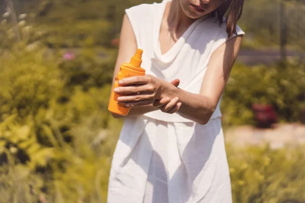 Una joven con un vestido blanco de verano se aplica gel protector solar en los brazos. —  Fotos de Stock