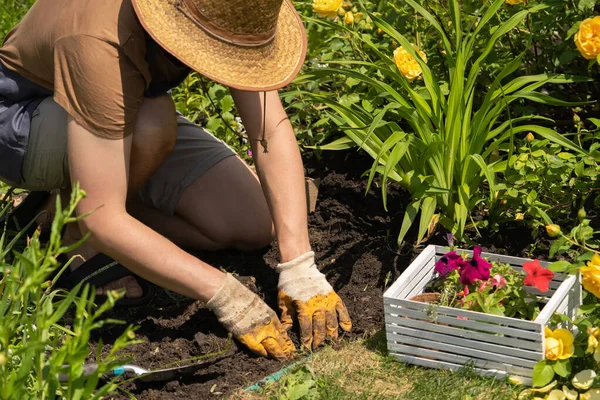 Um menino em um chapéu de palha e mãos em luvas está envolvido em trabalho de jardinagem — Fotografia de Stock