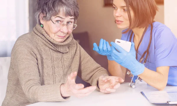 Uma enfermeira em um terno médico cuida e explica a um paciente idoso — Fotografia de Stock