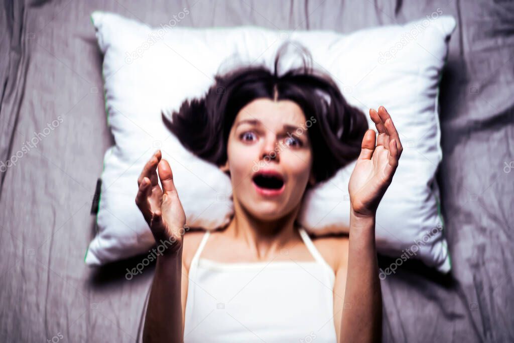 Young girl with a frightened expression wakes up from a nightmare in bed.