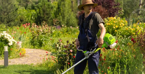 En ung man med gräsklippare tar hand om gräset på bakgården.. — Stockfoto