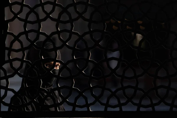 Tajemnicza dziewczyna w hidżabie stoi za ozdobnym kutym żelazem. — Zdjęcie stockowe