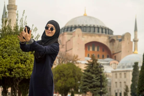 Молодая улыбающаяся мусульманка в хиджабе и стильных черных очках делает. — стоковое фото