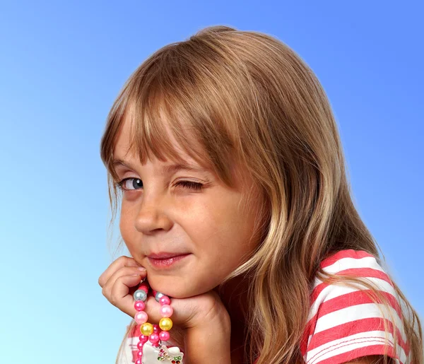 Little girl with beads winks and posing over blue background — 图库照片