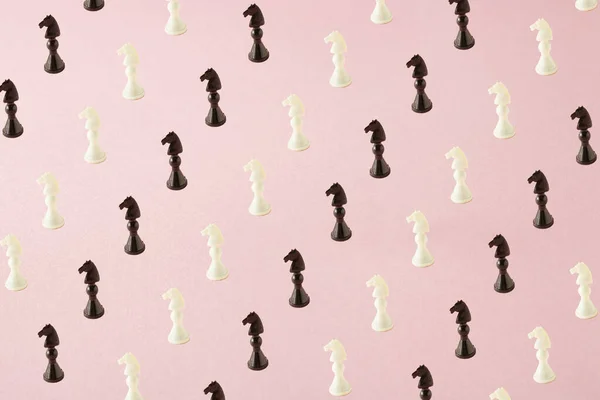 Chess pattern of black and white horses on pink background. Minimal lay out.