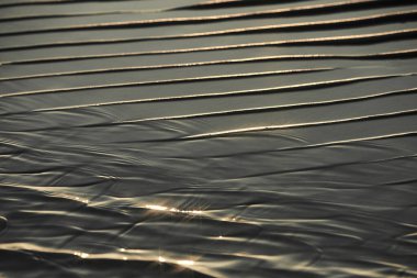 Kum dalgalarının dokusu deniz sahilinde suyla birlikte. Arkaplan için sarı kum dokusu.