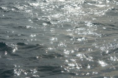 Parlak denize yansıyan güneş ışığının ayrıntıları. Suda maytap - arka plan. Güneş parlayan ve dalgalanan deniz suyu. Güçlü ve barışçıl doğa kavramı.