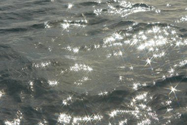 Parlak denize yansıyan güneş ışığının ayrıntıları. Suda maytap - arka plan. Güneş parlayan ve dalgalanan deniz suyu. Güçlü ve barışçıl doğa kavramı.