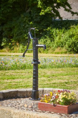 Eski siyah sokak su pompası. Genellikle bu tür pompaların suyu içilebilir değildir. Arka planda ve farklı renklerde binalar var..