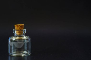 Siyah arka planda tıpası olan küçük cam kavanoz.