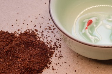 Açık renkli geri dönüşümlü kağıtta, kâsenin yanında kahverengi kahve tozu. Fotoğrafı kapat.