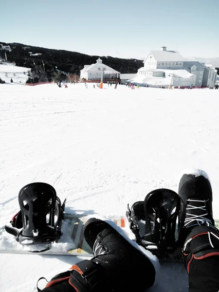 Bu fotoğrafta, snowboard sporuna ara veren birini görebilirsiniz. Karlı bir tatil köyü manzarası var ve diğer insanlar karın tadını çıkarıyor.