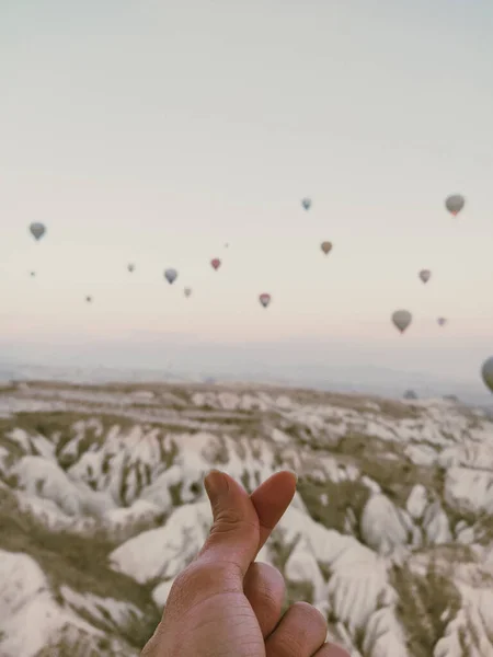 Bir aşk işareti el ve balonların arasından gökyüzünü işaret ediyor.