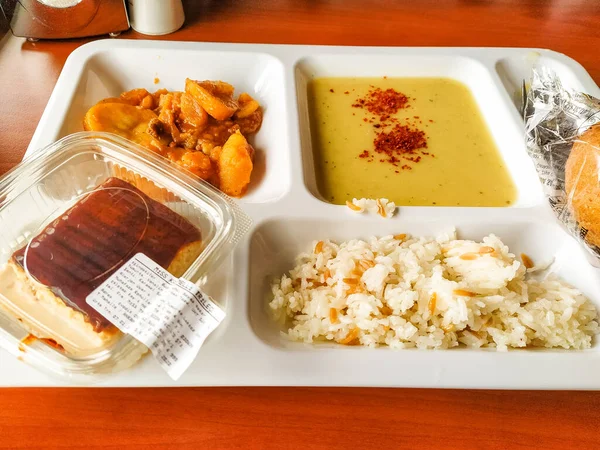 Ekmek, çorba, pirinç ve patates sosu ve tatlı içeren bir kampüs yemek takımı. Kahverengi, beyaz...