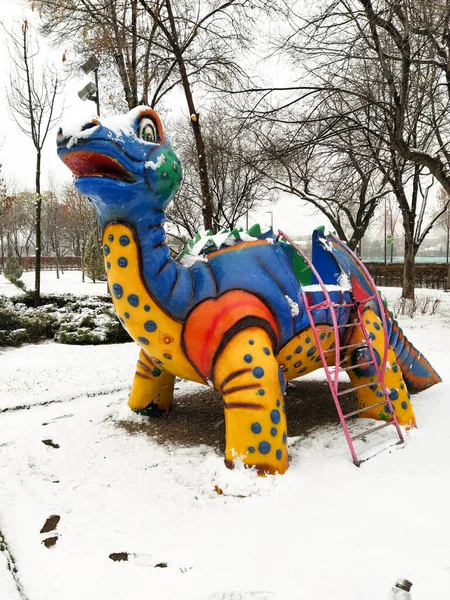 Beyaz, mavi, sarı, karlı parkta dinozor kayması.