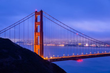 Battery Spencer 'ın siluetli tepesinin üzerindeki Golden Gate Köprüsü şafak vakti mavi bulutlu gökyüzü, San Francisco, California, ABD.