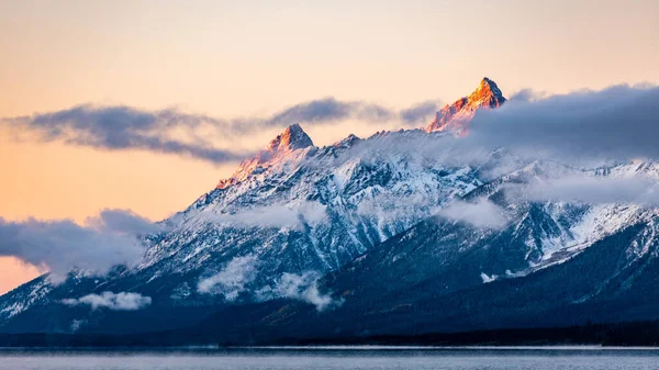 ABD 'nin Wyoming şehrinde, güneş doğarken bulutlarla kaplı Grand Teton dağlarının tepesinde kar yağdı..