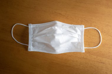 Kahverengi ahşap masada tek kullanımlık beyaz ameliyat maskesi..