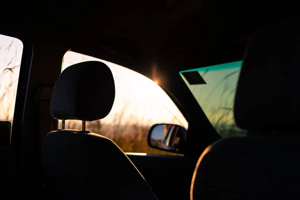 Abstract relax scene of silhouetted car seat with sunlight shining through opening window at sunrise. Blurry outdoor background is brown grass field of tropical rainforest at summer.