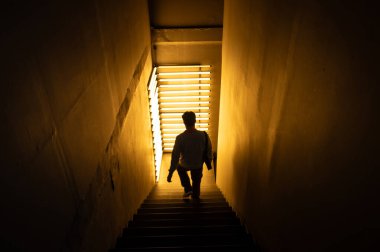 Bilinmeyen adam, köşedeki parlak sarı ışıkla dekore edilmiş eski karanlık binanın içindeki merdivenlerden aşağı iniyor..