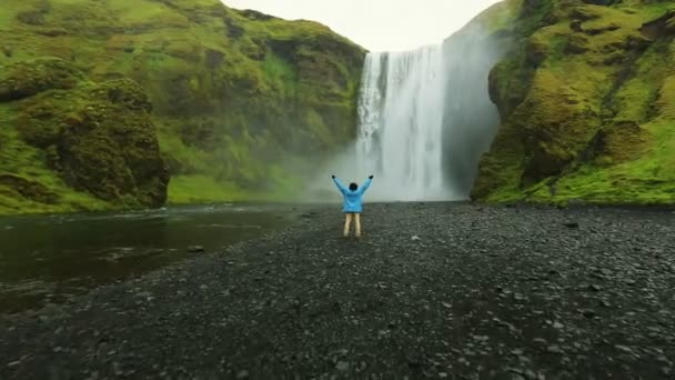 Jovem turista de sucesso em pé na frente da cachoeira. Skogafoss. — Vídeo de Stock
