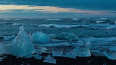 Siyah kum plajda küçük buzdağları günbatımı zaman atlamalı