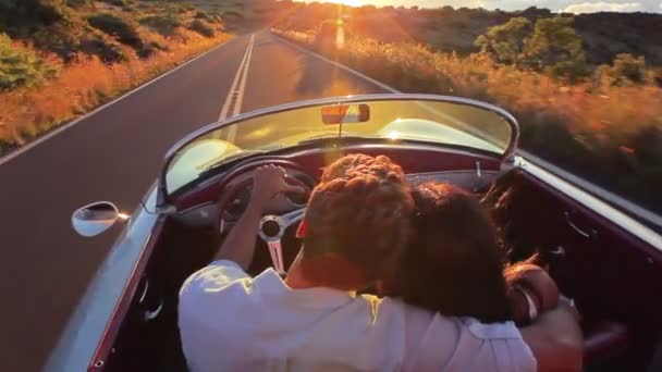 Casal feliz dirigindo carro conversível clássico em pôr do sol na estrada do país — Vídeo de Stock